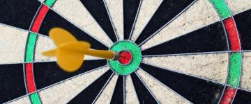 A close-up of a dartboard with a yellow dart stuck perfectly in the bullseye (FlitsArt/Pixabay).