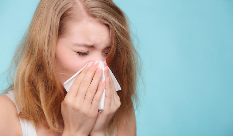 A sick girl sneezing in a tissue. 